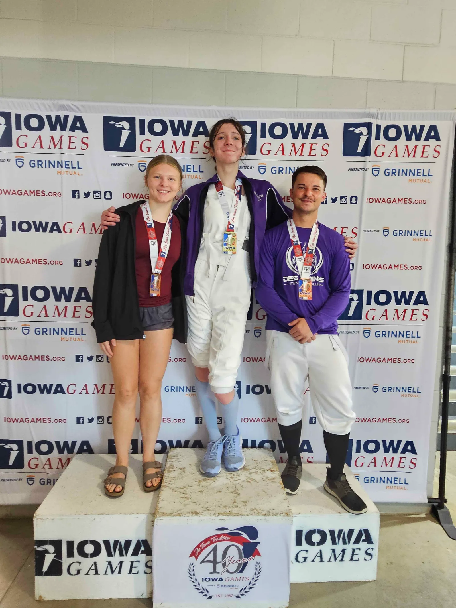 Three medalists pose on the podium in front of the Iowa Games 40th-anniversary backdrop.