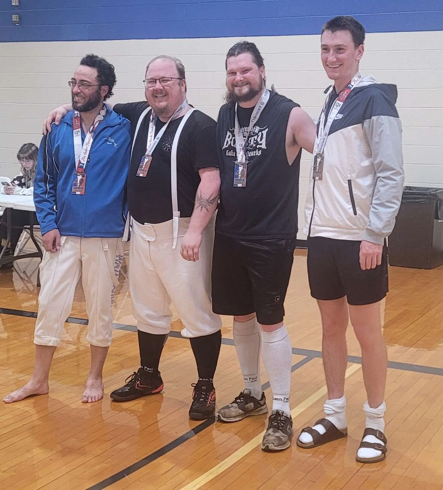 Four fencers stand shoulder to shoulder in the gym wearing their Iowa Games medals.