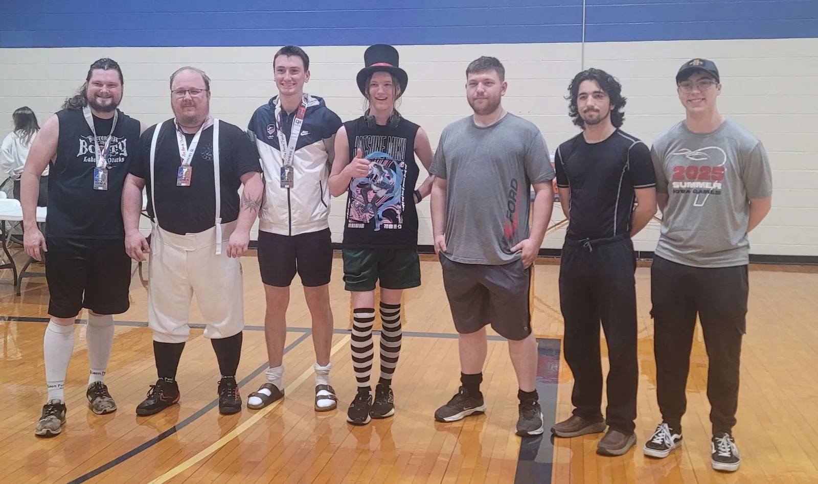 Seven fencers line up across the gym floor at the end of the day, one sporting a top hat.
